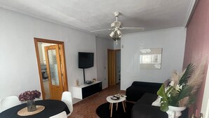 Una sala de estar con una mesa de comedor, sillas, un sofá, una mesa de centro, un televisor y un ventilador de techo.