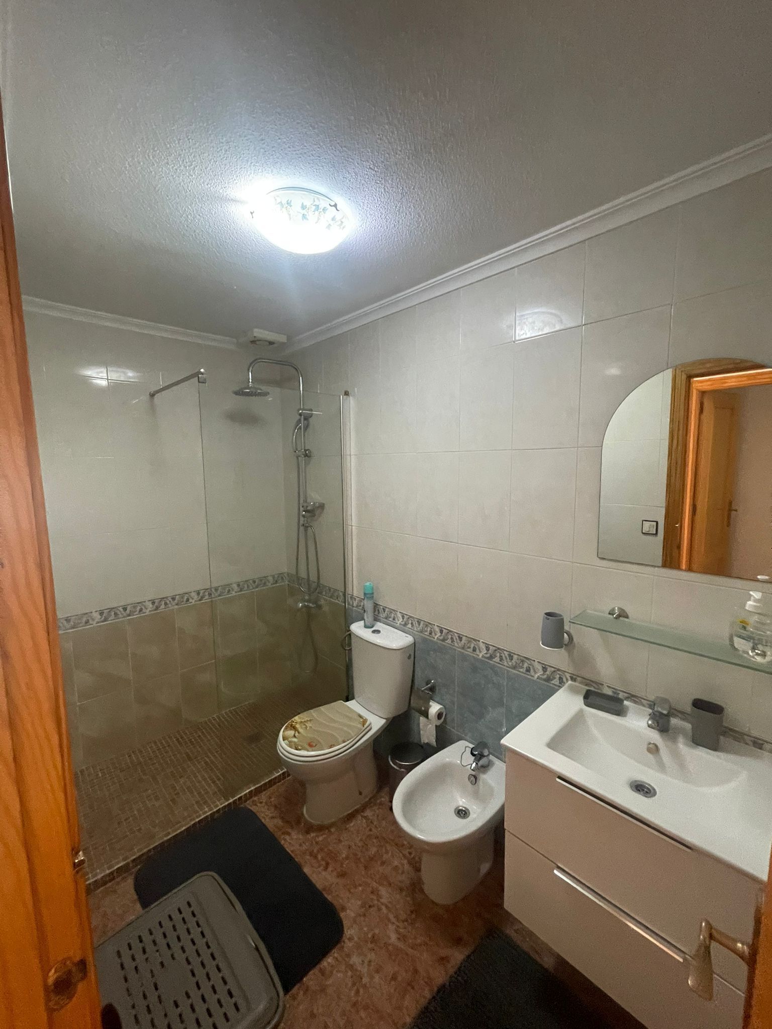 A bathroom with a shower, toilet, bidet, sink, and mirror.