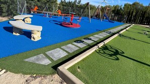 Un parque infantil con suelo de goma azul, columpios rojos y un tobogán.