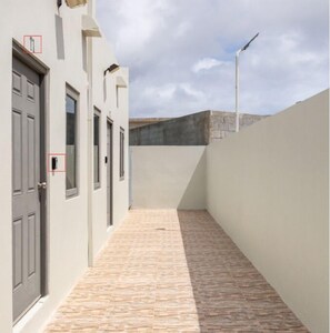 Stroll through this serene corridor, lined with light-colored walls and a grey door, leading to a tranquil outdoor space.