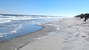 Ein Strand mit Wellen, blauem Himmel und Holzhütten rechts.