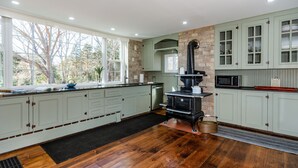 A spacious kitchen with a wood stove, a microwave, and a large window overlooking a tree. - Coastal Farmhouse at Ninigret Pond - 3.1 Mi to beach - Sleeps 4-12 people (Charlestown)