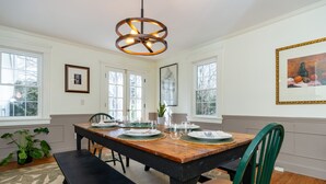 A dining area with a wooden table set for four, surrounded by chairs, a bench, and a hanging light fixture. - Coastal Farmhouse at Ninigret Pond - 3.1 Mi to beach - Sleeps 4-12 people (Charlestown)