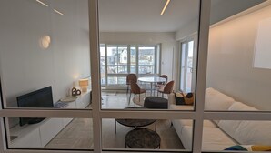 A modern living room with a TV, seating area, and a balcony with a view of the city. - Loving cocoon with furnished balcony (Les Sables-d'Olonne)