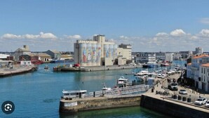 A marina with boats, a large building with murals, and a clear sky. - Loving cocoon with furnished balcony (Les Sables-d'Olonne)
