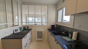 A modern kitchen with black countertops, white cabinets, and a large window providing a view of the city. - Loving cocoon with furnished balcony (Les Sables-d'Olonne)
