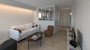 A modern living room with a white sofa, a brown armchair, a coffee table, and a TV stand with a monitor. - Loving cocoon with furnished balcony (Les Sables-d'Olonne)