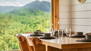 A dining table set with plates, bowls, and glasses, overlooking a mountainous landscape.