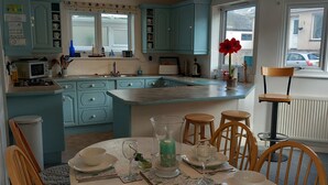Een keuken met blauwgroene kastjes, een eettafel gedekt met borden, glazen en een karaf.