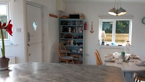 Een keuken met een eettafel voor vier personen, een boekenkast en een raam met uitzicht op groen.