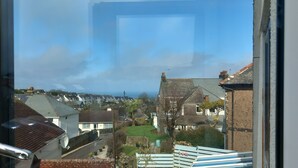 Een woonwijk met huizen, een heldere lucht en een uitzicht door een raam met een metalen handgreep.