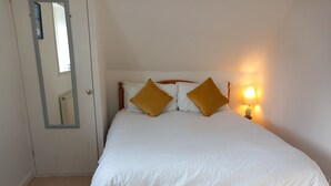 Een bed met witte lakens en twee gouden kussens, een bedlampje en een spiegel aan de muur.