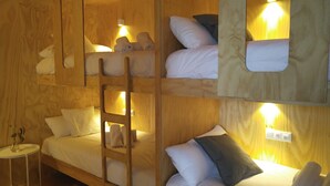 A multi-level wooden room with bunk beds, a ladder, and bedside lamps. - Area Surf House (Muros)