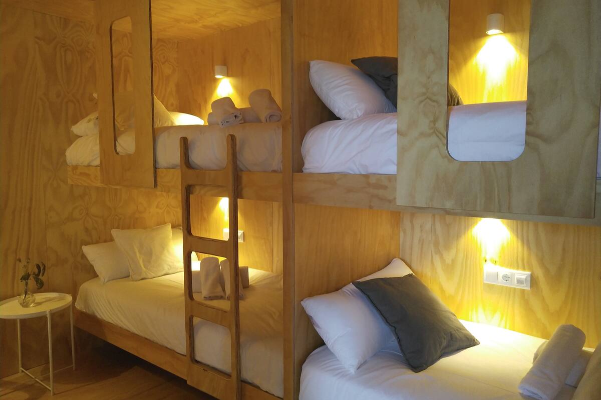 Una habitación de madera con varios niveles, literas, una escalera y lámparas de noche.