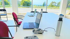A conference room with a white table, two laptops, a portable gaming console, and a water bottle. - Area Surf House (Muros)