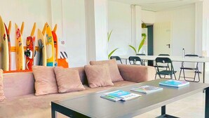 A modern living room with a sofa, coffee table, and surfboards on display. - Area Surf House (Muros)