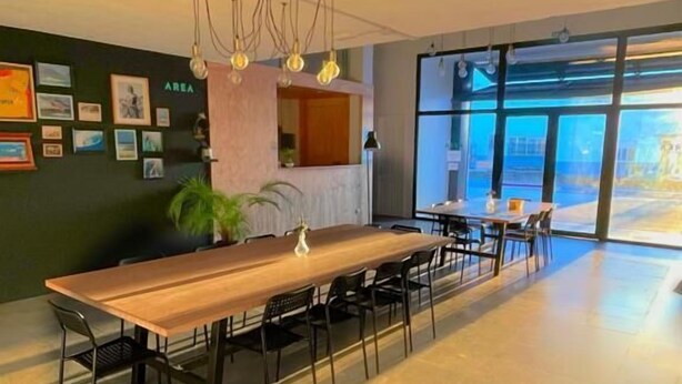 A spacious dining area with a long wooden table, black chairs, and a modern chandelier. - Area Surf House (Muros)