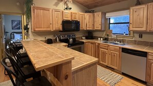 Une cuisine avec des meubles en bois, un îlot central, des tabourets de bar, un four à micro-ondes, une cuisinière et un lave-vaisselle.