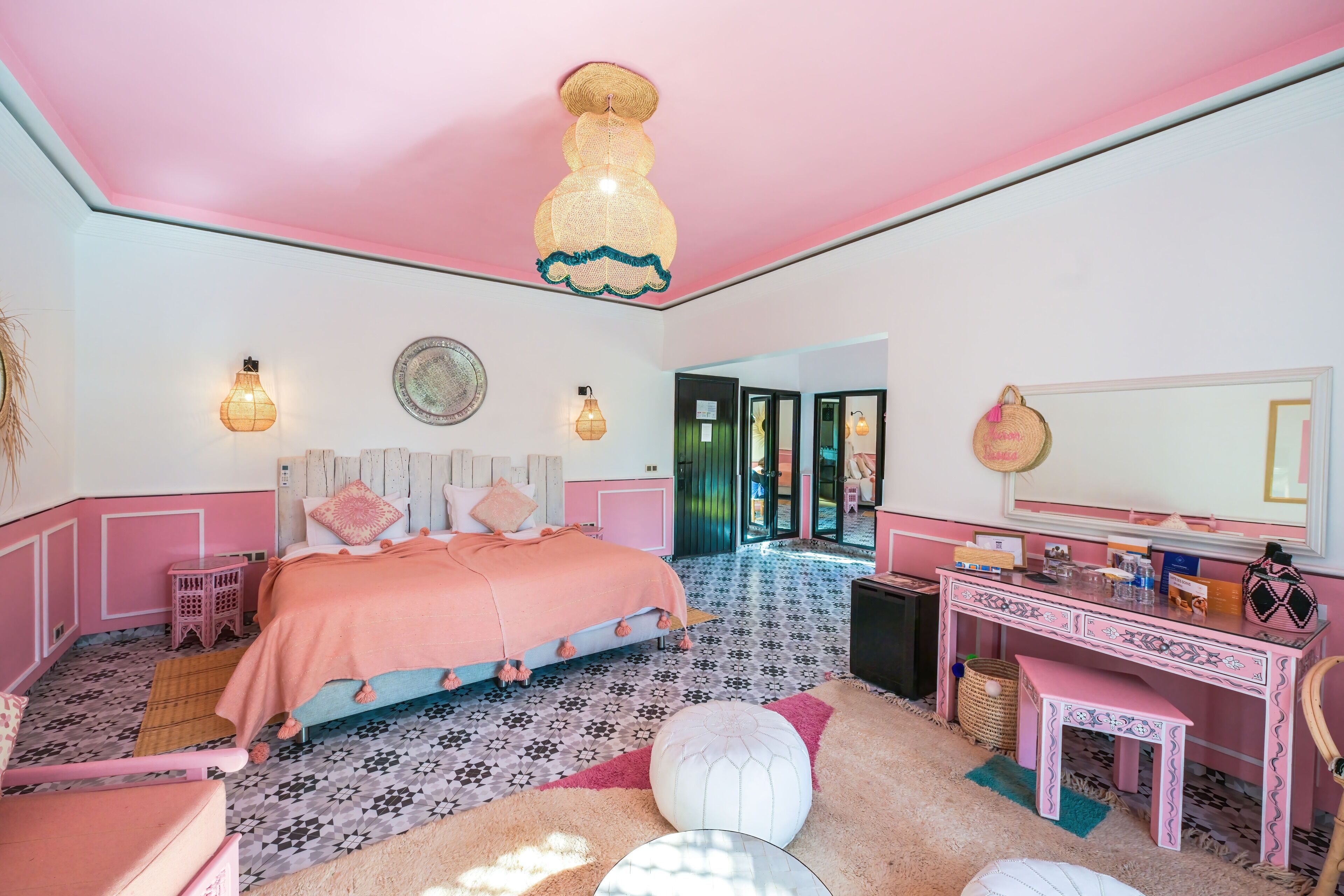 Un dormitorio rosa con cama, mesita de noche y escritorio con espejo.