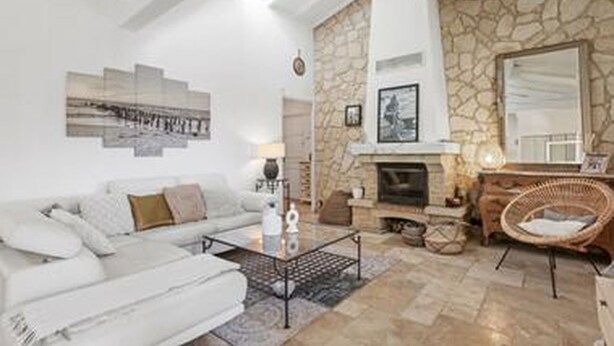 Una sala de estar moderna con una chimenea de piedra, un sofá blanco y un sillón de mimbre.
