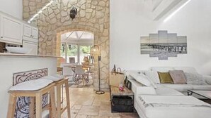 Un interior moderno con un arco de piedra que conduce a un comedor, un sofá con cojines y una cama con cabecera blanca.