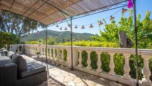 Un patio exterior con zona de estar cubierta, suelo de piedra y barandilla decorativa.