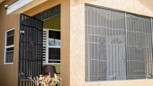A building with barred windows and a door, a small balcony, and a chair visible inside. - Captivating 2-bed House in Falmouth (Falmouth)
