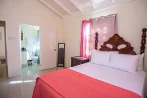 Une chambre à coucher avec un lit, une tête de lit en bois, une table de chevet, un miroir et une salle de bain visible à travers une porte ouverte.