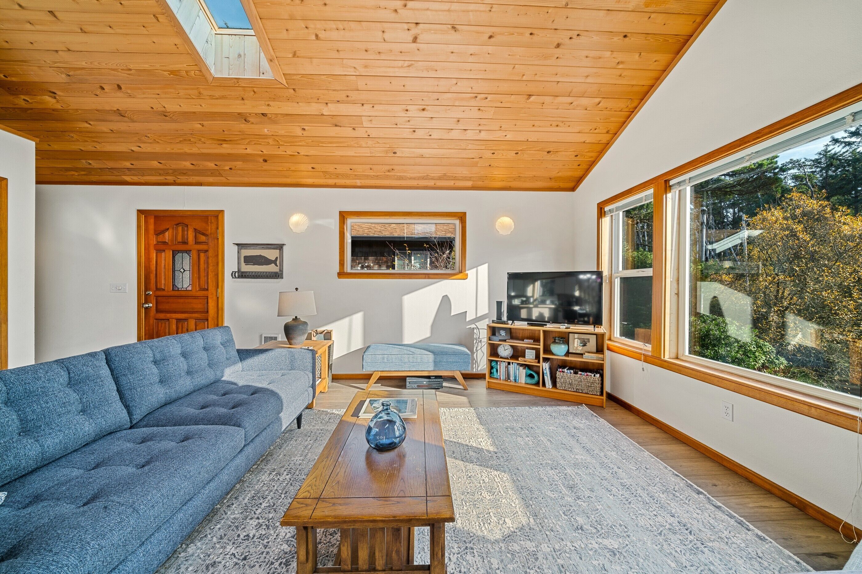 Una sala de estar moderna con techo de madera, un ventanal grande, un sofá, una mesa de centro y un televisor.