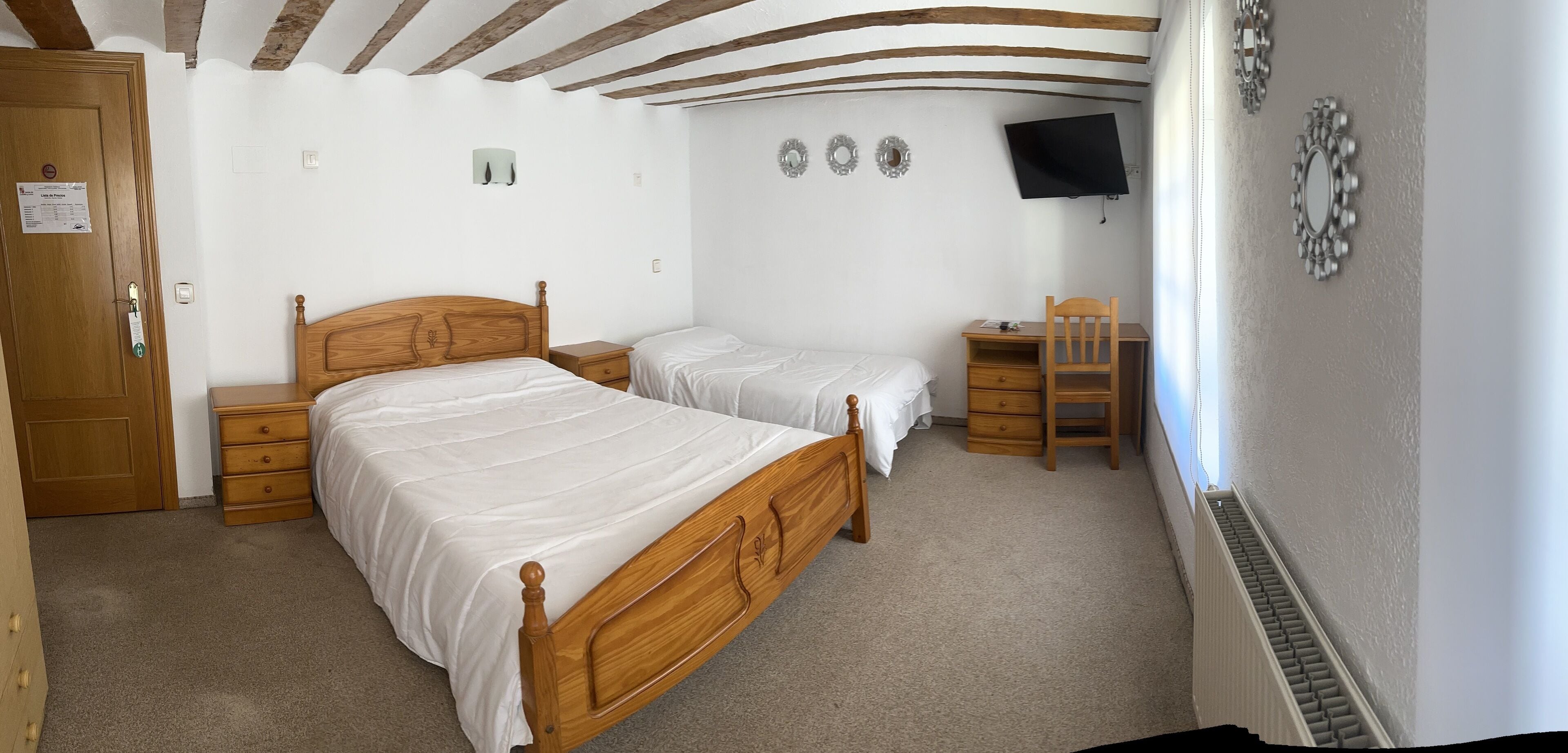 Una camera da letto con due letti in legno, una scrivania, una sedia e una TV a parete.