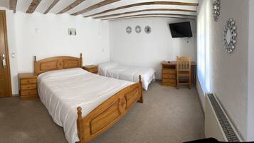 A bedroom with two wooden beds, a desk, a chair, and a TV mounted on the wall.