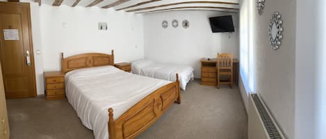Un dormitorio con dos camas de madera, un escritorio, una silla y un televisor instalado en la pared.