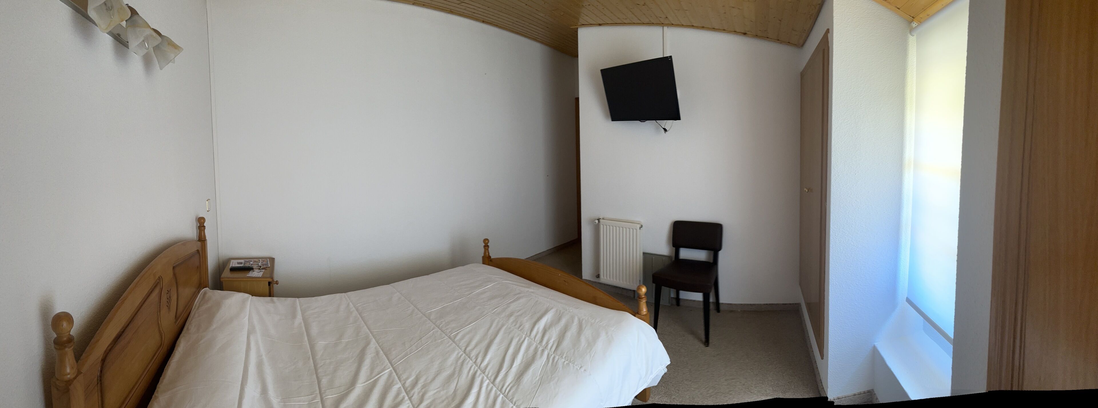 Een slaapkamer met een enkel bed, een stoel, een radiator en een aan de muur bevestigde televisie.