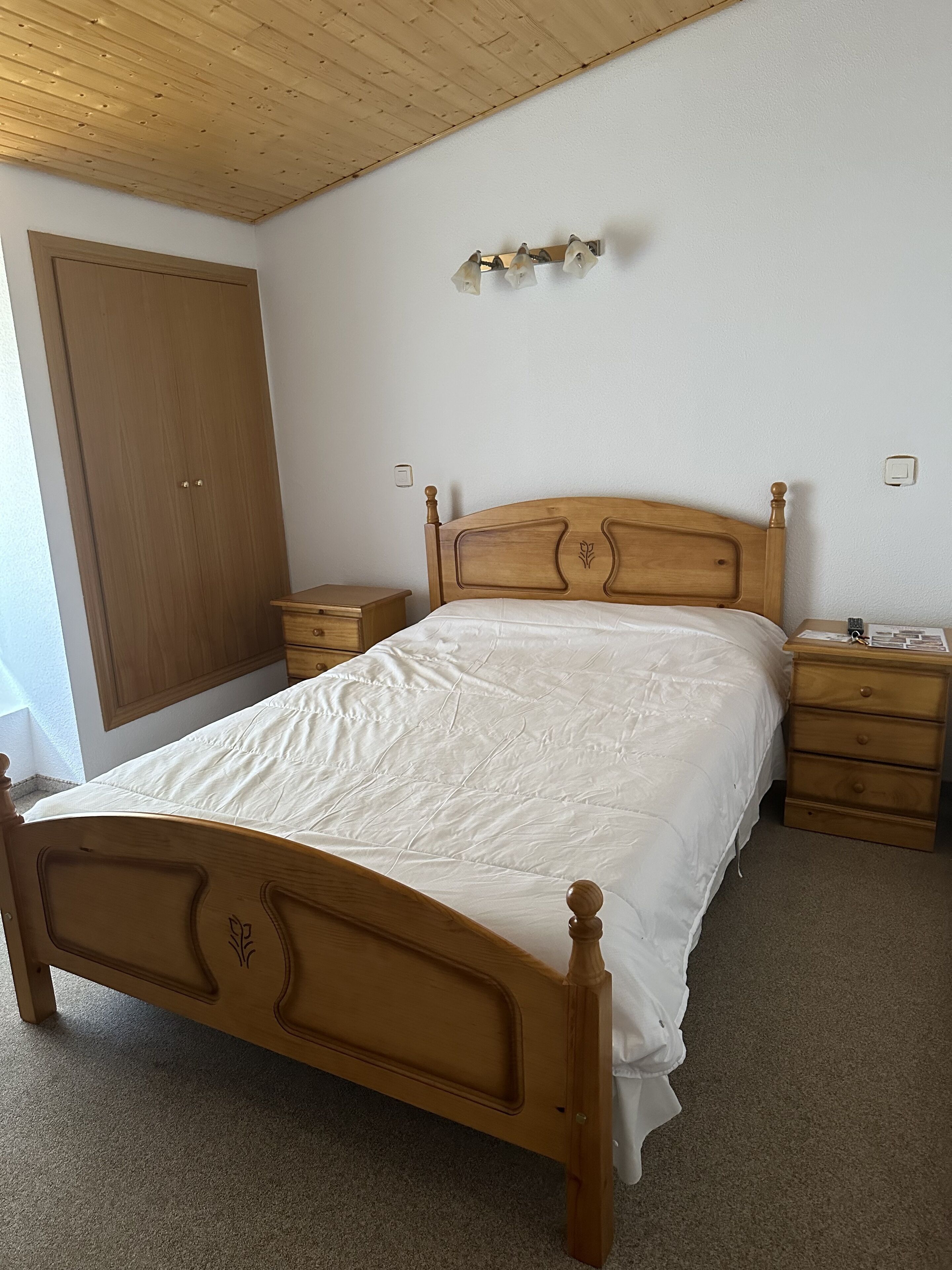 A bedroom with a wooden bed, a nightstand, a dresser, a wardrobe, and a ceiling light fixture.
