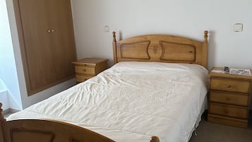 A bedroom with a wooden bed, a nightstand, a dresser, a wardrobe, and a ceiling light fixture.