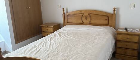 Egy hálószoba, amelyben van egy faágy, egy éjjeliszemélyzet, egy komód, egy szekrény és egy mennyezeti lámpatest.