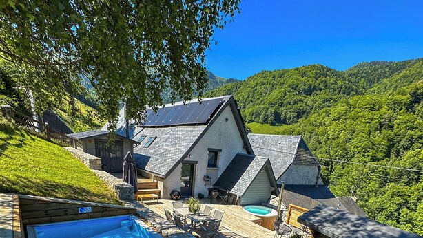 Eine Holzterrasse mit Whirlpool, Sitzgelegenheiten im Freien und Blick auf einen Berg.