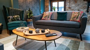 Ein gemütliches Wohnzimmer mit einer Couch, einem Sessel, einem Holztisch mit Tablett und Fernbedienung sowie einem Weihnachtsbaum.