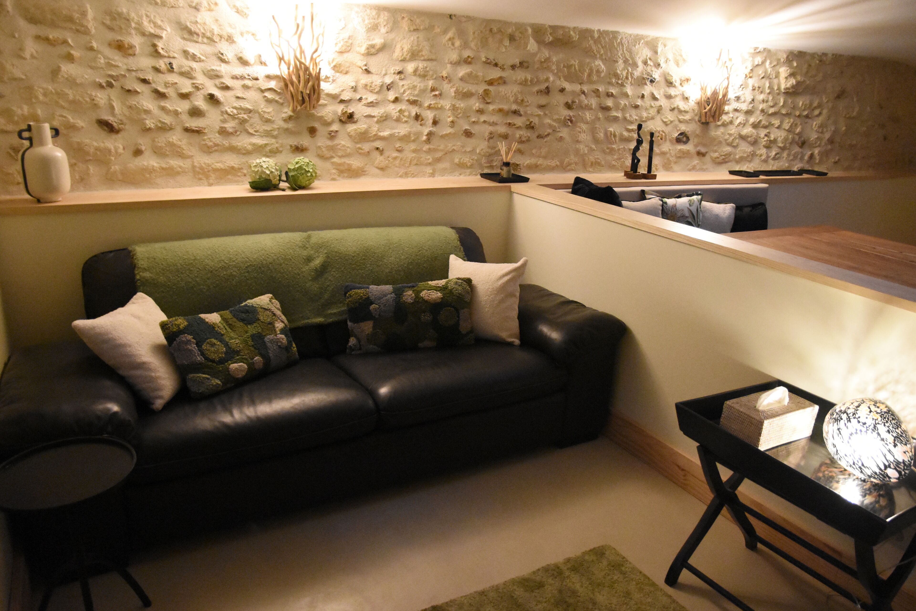 A living room with a black leather sofa, a glass coffee table, and a stone wall.