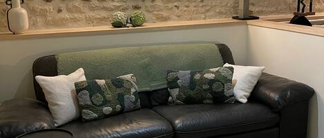 A modern living room with a stone wall, a black leather sofa, and a small side table.