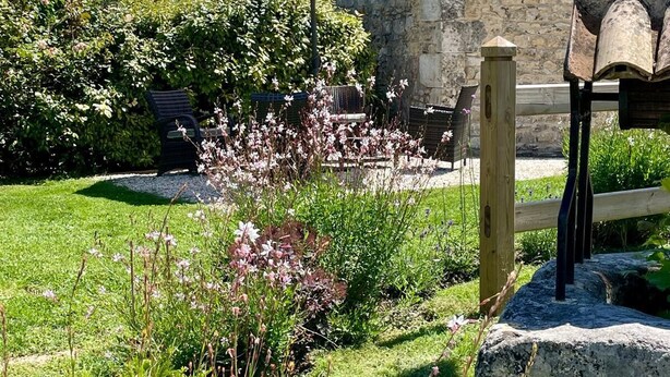 A stone building with a tiled roof, a wooden fence, and a garden with various plants and flowers. - Les Girauderies Chambres d'Hotes  (Floirac)