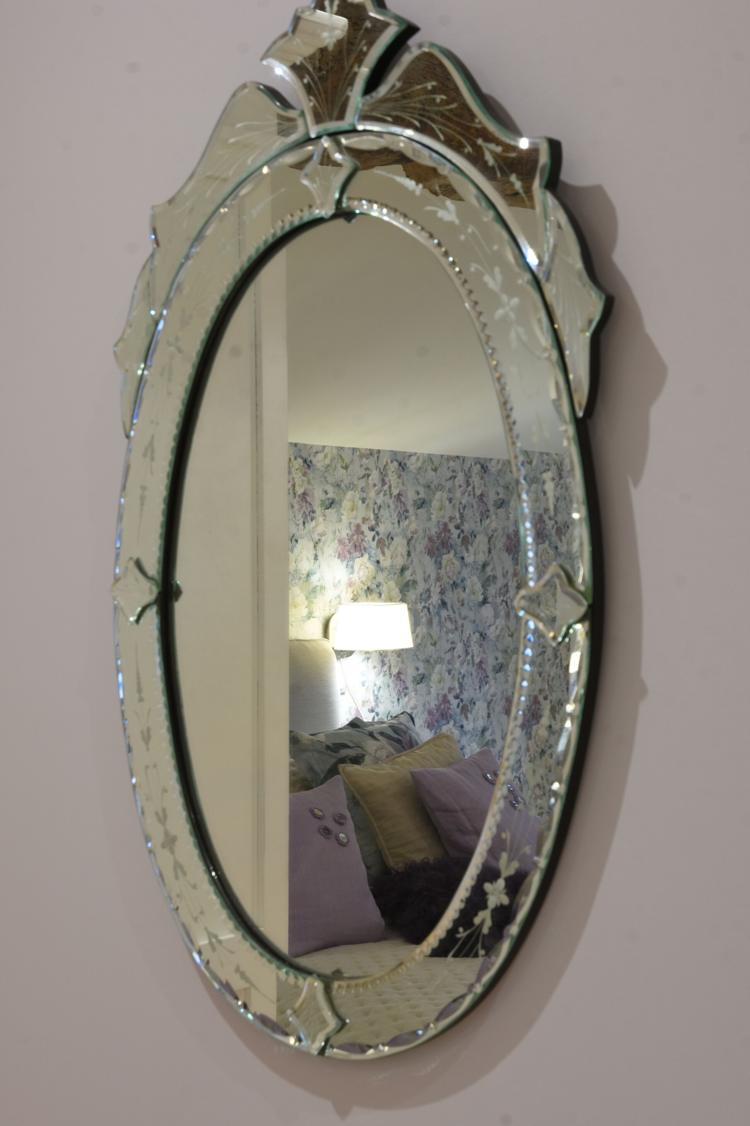 Een decoratieve ovale spiegel met een bloemmotief aan de muur.