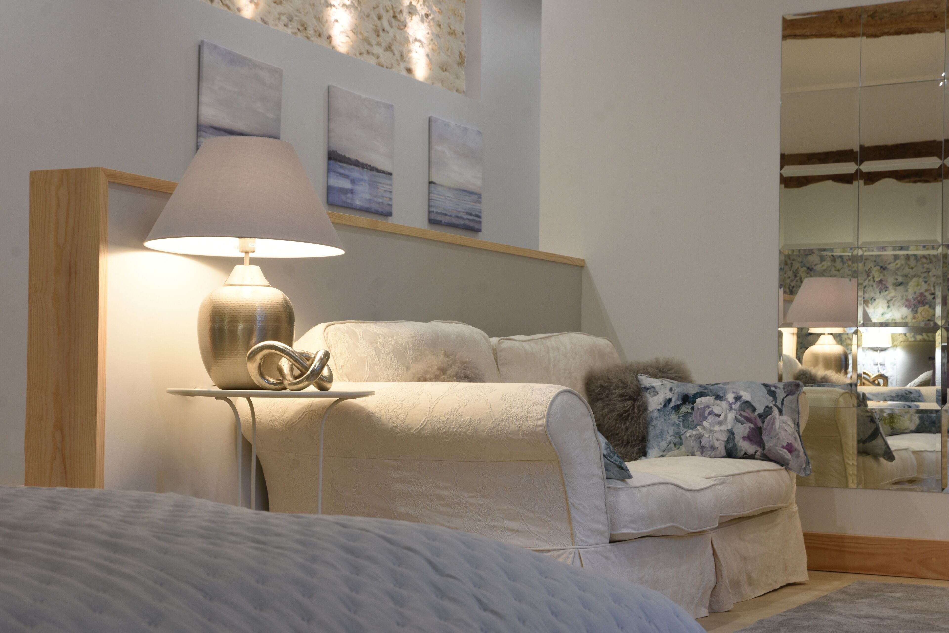 Un dormitorio con cama, lámpara de noche, mesita de noche, espejo y una obra de arte en la pared.