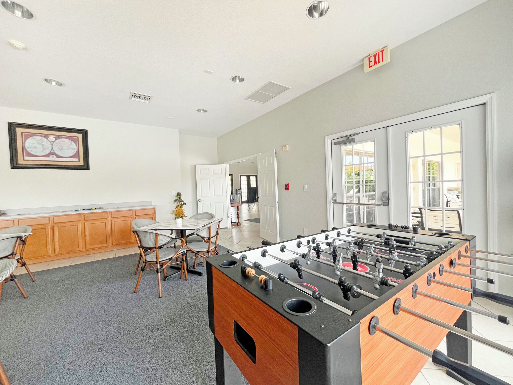 A room with a foosball table, a dining table with chairs, and a framed picture on the wall.