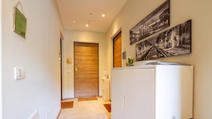 Un couloir avec une porte en bois, un réfrigérateur blanc et un cadre photo fixé au mur.