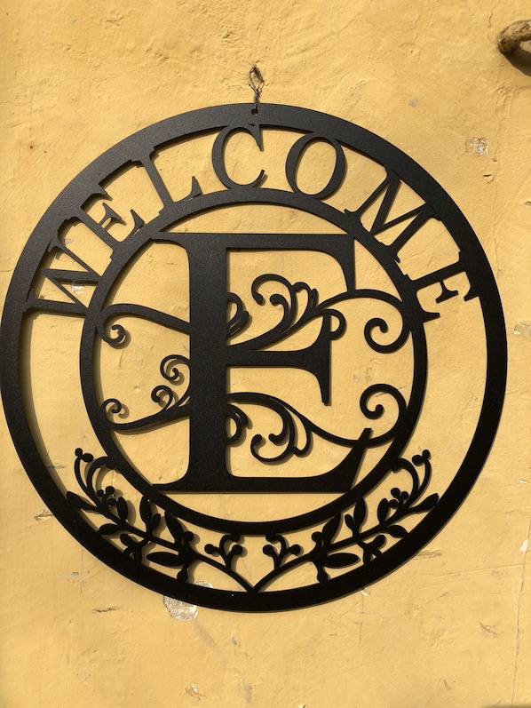 A circular metal sign with the word "WELCOME" and a large letter "E" in the center, mounted on a yellow wall.