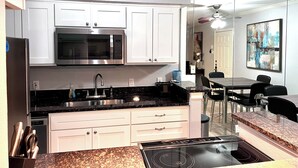 A modern kitchen with white cabinets, a built-in microwave, a stainless steel sink, and a granite countertop. - I40 - Apt|Patio|11mi to Convention Ctr|Sleeps 2 (Irving)