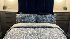 A bed with a floral-patterned bedspread, a tufted headboard, and bedside tables with lamps and potted plants. - Modern house with a Tub!!! (Bangor)