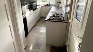 A modern kitchen with white cabinetry, a central island with a stove, and a window providing natural light. - Modern house with a Tub!!! (Bangor)