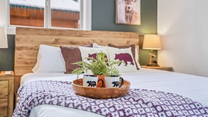 A neatly made bed with a patterned blanket, a wooden headboard, and a bedside table with a lamp. A wooden tray with two mugs and a plant is on the bed. - Golf Course views, Deer in yard, Next to Lake (McCall)